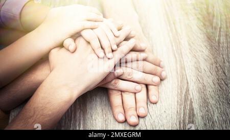 Famille heureuse tenant les mains à la table en bois à l'intérieur, gros plan. Bannière Banque D'Images