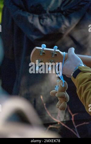 Une verticale d'un petit ours en peluche accroché à la tête d'une guitare dans la main d'un homme Banque D'Images