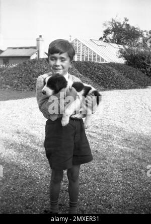 1950s, historique, à l'extérieur, un jeune écolier heureux tenant dans les bras son petit chien de compagnie, une frontière tachetée collie, Angleterre, Royaume-Uni. Banque D'Images