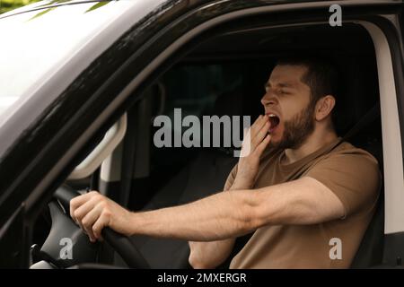 Un homme fatigué bâilling en conduisant sa voiture moderne Banque D'Images