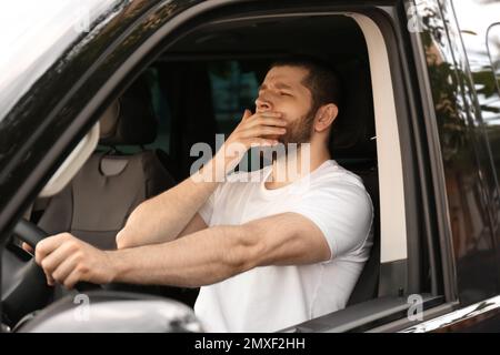 Un homme fatigué bâilling en conduisant sa voiture moderne Banque D'Images