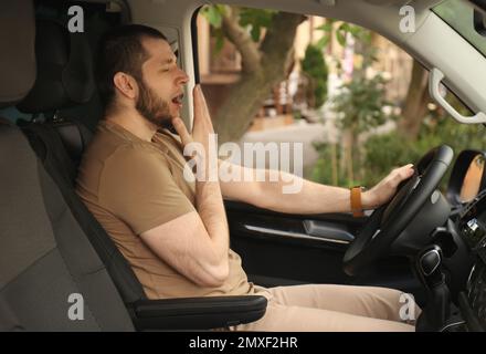 Un homme fatigué bâilling en conduisant sa voiture moderne Banque D'Images