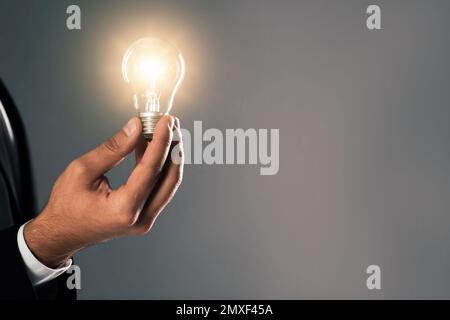 Concept d'idée. Homme d'affaires avec ampoule lumineuse sur fond gris, gros plan Banque D'Images