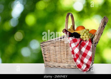 Panier pique-nique en osier avec vin et différents fruits sur table à l'extérieur, espace pour le texte Banque D'Images