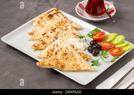 Pain plat turc traditionnel ou Gozleme avec tomates, olives et thé sur table en pierre sombre Banque D'Images