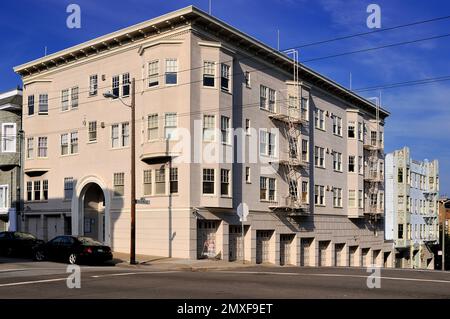 Immeuble d'appartements beige classique avec évasions de feu lors d'une journée ensoleillée à San Francisco. Terrain d'angle avec architecture historique, ombres et ciel bleu. Banque D'Images