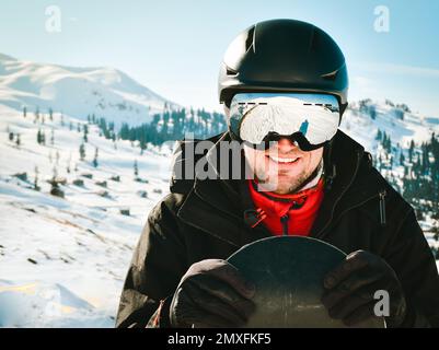 Gros plan portrait homme caucasien avec le reflet des montagnes neigeuses, de la pente blanche et de la station de ski. Une chaîne de montagnes reflétée dans le masque de ski. Port Banque D'Images