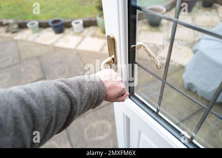 Propriétaire ouvrant la porte à double vitrage au plomb à l'arrière, récemment installée, menant à un jardin arrière et une terrasse. Banque D'Images