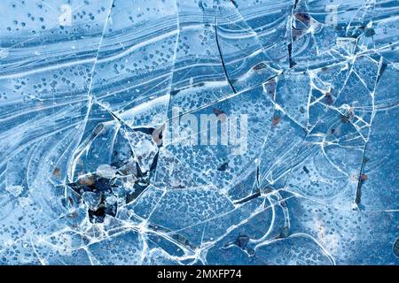 Gros plan montrant la surface fissurée et cassée d'une flaque couverte de glace, les motifs abstraits déformés et de travers. Banque D'Images