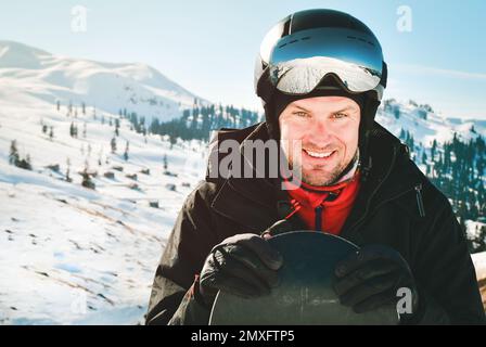 Gros plan portrait homme caucasien avec le reflet des montagnes neigeuses, de la pente blanche et de la station de ski. Une chaîne de montagnes reflétée dans le masque de ski. Port Banque D'Images