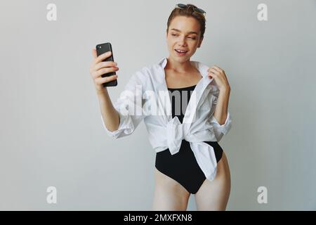 Une jeune fille blogger prend des photos et des pousses. elle-même sur la vidéo sur son téléphone pour le contenu de médias sociaux, blogueur vidéo, se selfie contre un mur blanc avec Banque D'Images