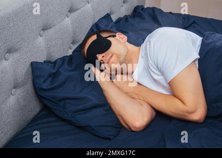 Vue de dessus d'un jeune homme portant un masque de sommeil reposant dans sa chambre. Détente, repos après le travail Banque D'Images