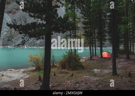 Une tente orange se dresse dans des épinettes sur la rive du lac de haute altitude Shavlinskoye en Altaï. Banque D'Images