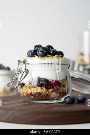 Petit déjeuner flocons d'avoine avec des fruits dans un pot en verre à base de yaourt grec et granola garni de myrtilles fraîches sur un tissu rayé avec cuillère à miel, santé Banque D'Images