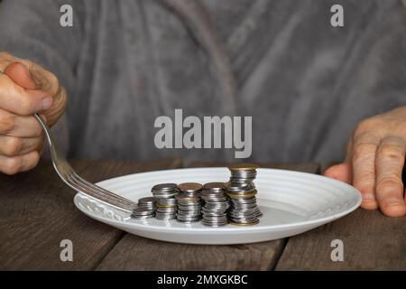une pile de pièces de monnaie sur une assiette blanche sur une ancienne table en bois et de vieilles mains de femmes ont versé une assiette à la maison dans la cuisine Banque D'Images