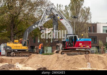 deux grosses pelles hydrauliques sur un chantier de construction avec une personne debout sur un tas de sable Banque D'Images