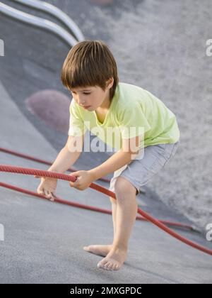 Garçon monte sur une pente de béton de sports et de terrain de jeu modernes pour enfants. Kid surmonte la peur et apprend de nouvelles choses. Activités de loisirs en plein air. Banque D'Images