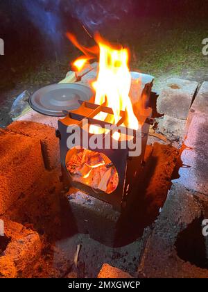 Le brûleur à bois brûle la nuit à côté du couvercle de la casserole. Banque D'Images