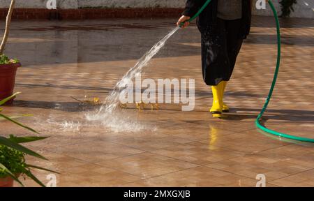 un homme inconnu verse l'eau d'un tuyau vert sur une tuile dans la cour Banque D'Images