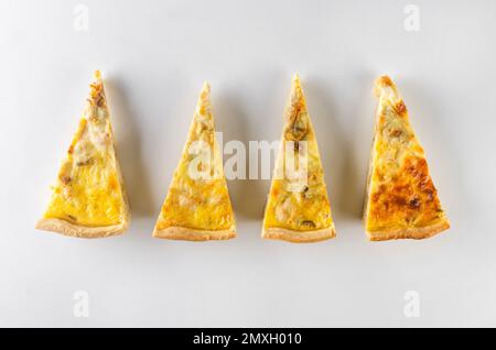 Quatre tranches ouvrent la tarte sur la table blanche. Quiche Lorraine maison avec poulet, champignons et fromage sur table blanche. Tarte maison, coupée en morceaux. Français Banque D'Images