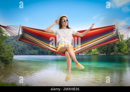 Femme se reposant dans un hamac près de la rivière et des montagnes le jour ensoleillé Banque D'Images