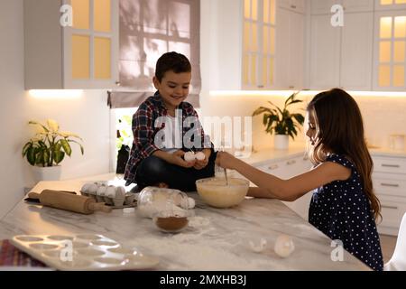 De jolis petits enfants cuisent de la pâte dans la cuisine à la maison Banque D'Images