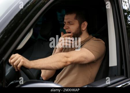 Un homme fatigué bâilling en conduisant sa voiture moderne Banque D'Images