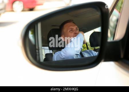 Un jeune homme fatigué bâillonant dans son auto, vue à travers le rétroviseur latéral de voiture Banque D'Images