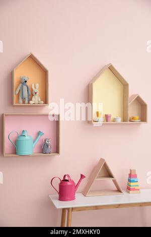 Étagères élégantes en forme de maison avec jouets et table en bois à l'intérieur. Décoration intérieure de la chambre de bébé Banque D'Images