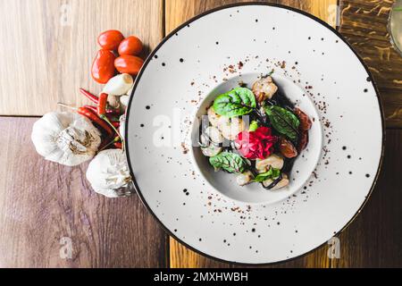 Vue de haut en bas du plat de pâtes noir tagliolini avec tomates séchées et crevettes servies sur une assiette blanche sur une table en bois décorée d'épices. Cuisine italienne. Prise de vue horizontale en intérieur. Photo de haute qualité Banque D'Images