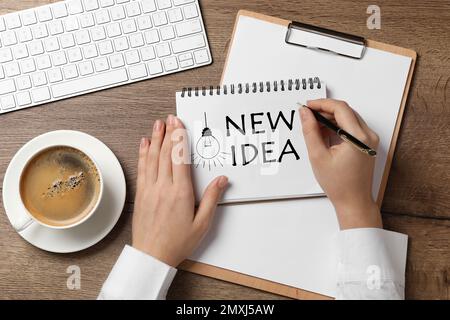 Femme écrivant des mots NOUVELLE IDÉE dans le carnet à table en bois, vue de dessus Banque D'Images
