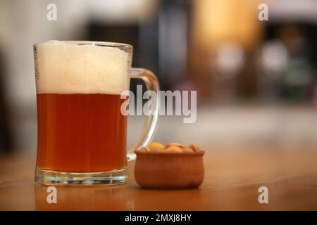 Pinte de bière fraîche savoureuse servie avec des arachides sur une table en bois Banque D'Images