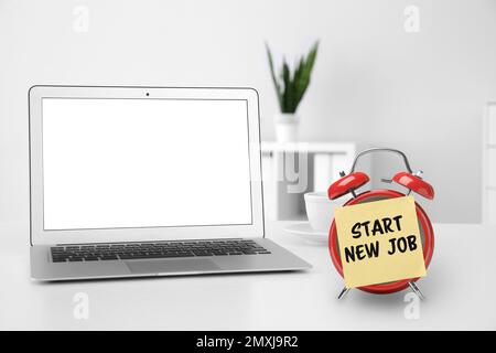 Autocollant avec texte commencer un nouveau travail sur un réveil près d'un ordinateur portable dans un bureau moderne Banque D'Images