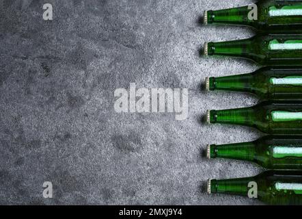 Bouteilles vertes avec bière sur table grise, plat. Espace pour le texte Banque D'Images