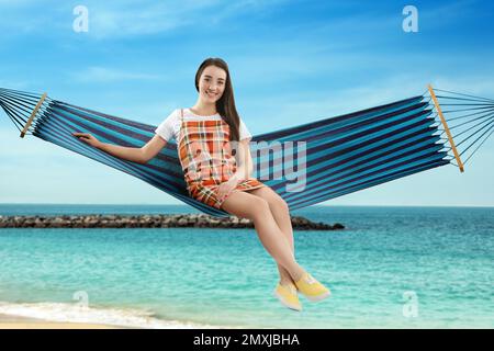 Femme se reposant dans un hamac près de la mer le jour ensoleillé Banque D'Images