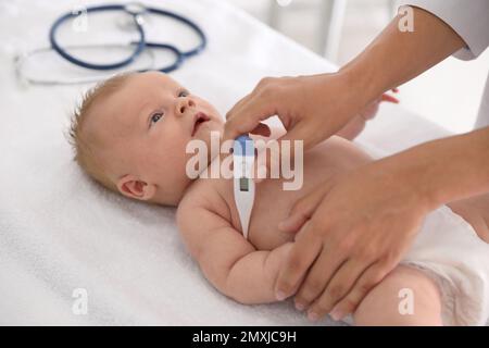 Médecin mesurant la température du bébé avec un thermomètre numérique à l'intérieur, gros plan. Soins de santé Banque D'Images