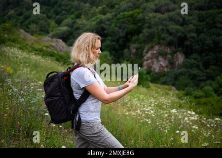 Femme randonneur utilise l'application de navigateur gps dans smartphone marchant dans la forêt, personne touriste regarde le téléphone mobile pour la navigation. Concept de randonnée, nature, pe Banque D'Images