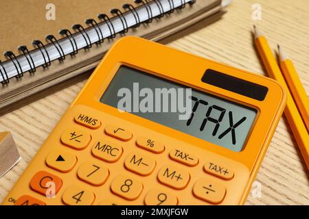 Calculatrice avec mot Tax, bloc-notes et crayons sur table en bois, gros plan Banque D'Images