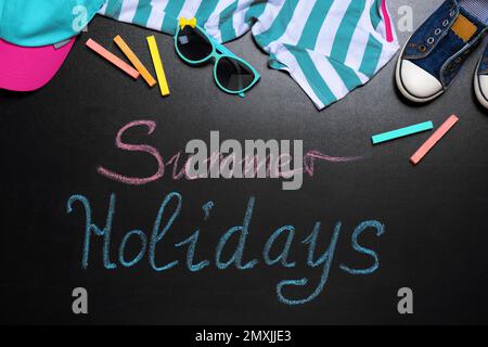 Composition de la pose à plat avec vêtements pour enfants et inscription Summer Holidays sur tableau noir. Pause-école Banque D'Images