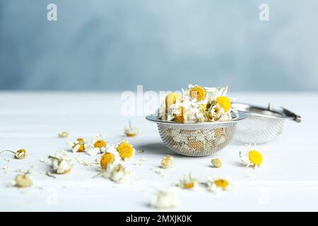 Sécher les fleurs de camomille dans l'infuser sur une table en bois blanc Banque D'Images