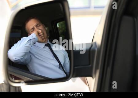 Un jeune homme fatigué bâillonant dans son auto, vue à travers le rétroviseur latéral de voiture Banque D'Images