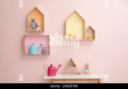 Étagères élégantes en forme de maison avec jouets et table en bois à l'intérieur. Décoration intérieure de la chambre de bébé Banque D'Images