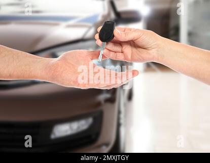 Achat de voiture. Femme donnant la clé au nouveau propriétaire contre l'automobile floue, gros plan Banque D'Images