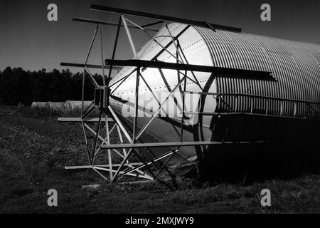 Un silo de métal tombé repose sur l'herbe avec une rangée de serres en arrière-plan sur une ferme. Littleton, Massachusetts. L'image a été capturée sur BL analogique Banque D'Images