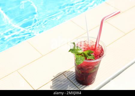 Délicieux rafraîchissement dans une tasse en plastique près de la piscine. Espace pour le texte Banque D'Images