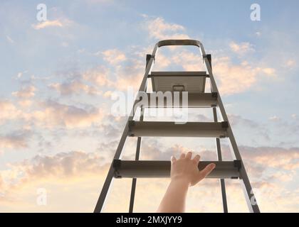 Femme grimpant sur un escabeau contre le ciel avec des nuages, gros plan Banque D'Images