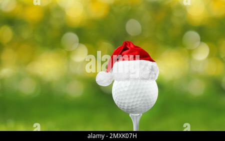 Balle de golf avec petit chapeau de père Noël sur le tee-shirt sur fond flou Banque D'Images