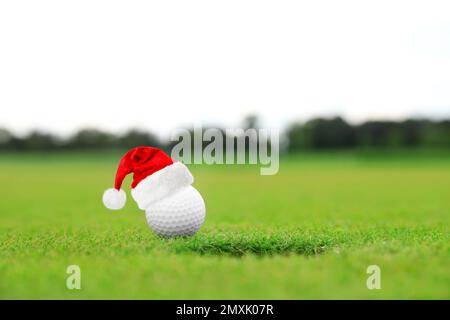 Balle de golf avec petit chapeau de père Noël près du trou sur le parcours vert Banque D'Images