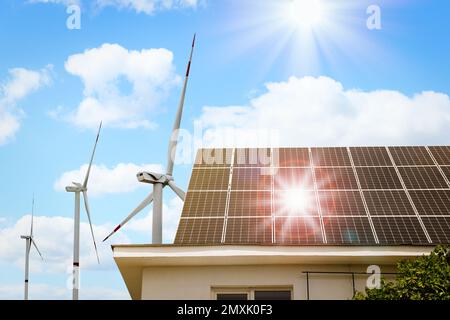 Éoliennes près de la maison avec panneaux solaires installés sur le toit. Source d'énergie alternative Banque D'Images