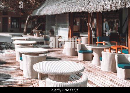 Vue sur une terrasse extérieure vide dotée de confortables sièges en osier de couleur crème avec coussins, parquet et toit de chaume rustique cr Banque D'Images